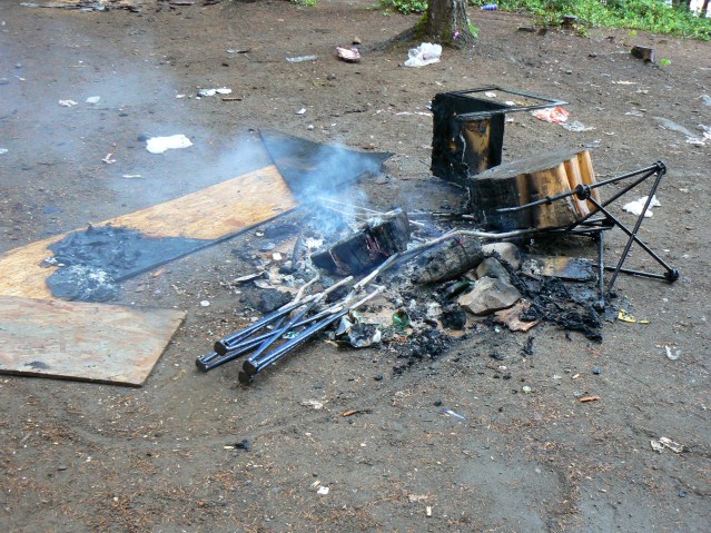 Campfire with burnt chairs and camp stools at Beavertail lake